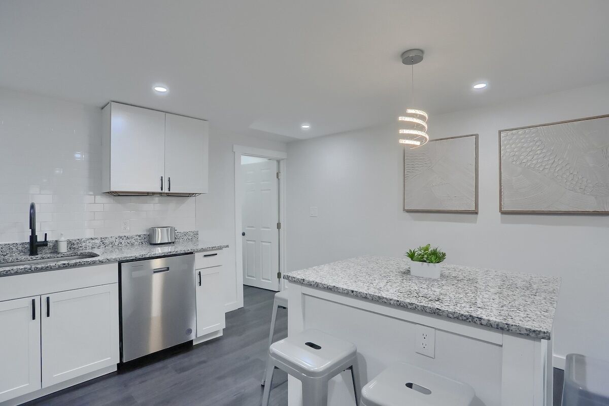A modern kitchen with white cabinets, a stainless steel dishwasher, granite countertops, and a pendant light.