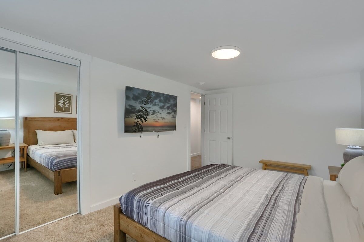 Quarto com cama, mesa de cabeceira, abajur, pintura e porta.