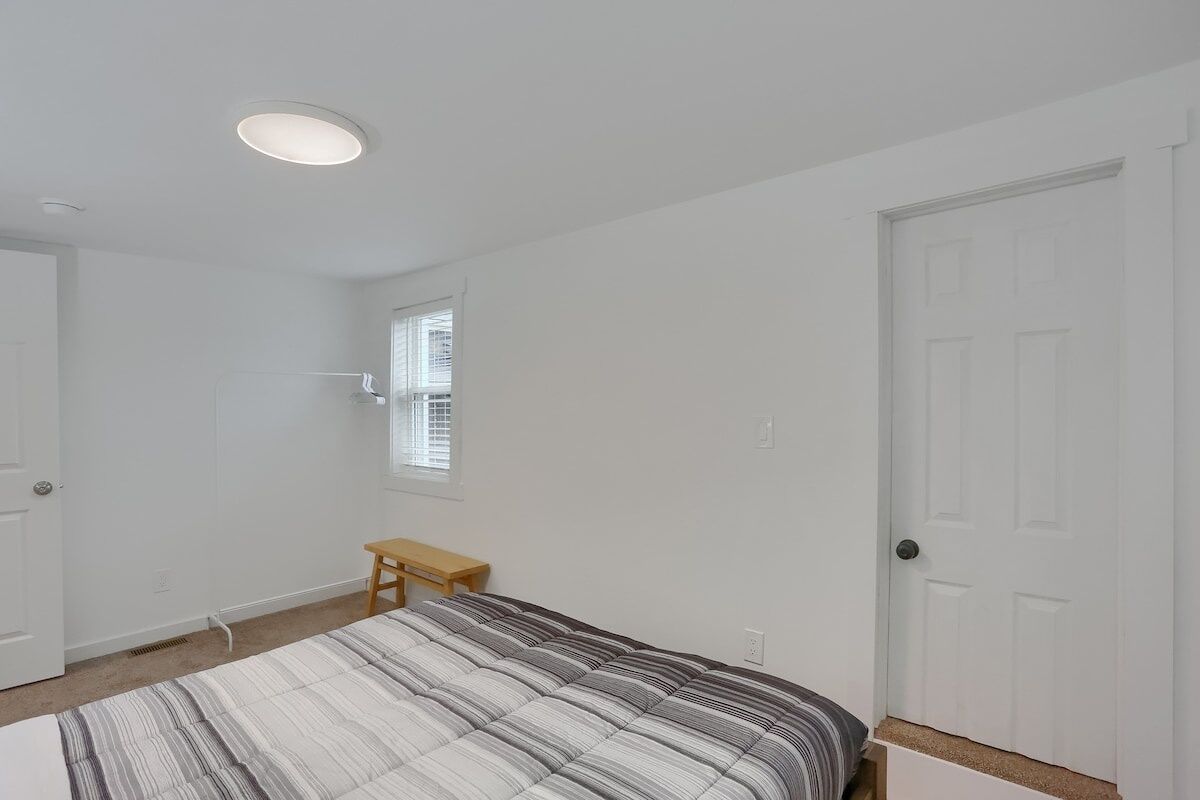 A bedroom with a bed, a window, a door, and a small wooden table.