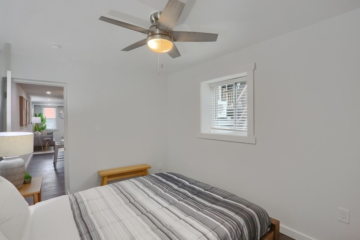 A bedroom with a bed, a ceiling fan, a window with blinds, and a small bench.