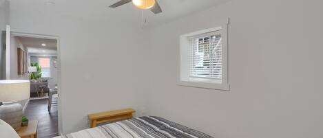 A bedroom with a bed, a ceiling fan, a window with blinds, and a small bench.