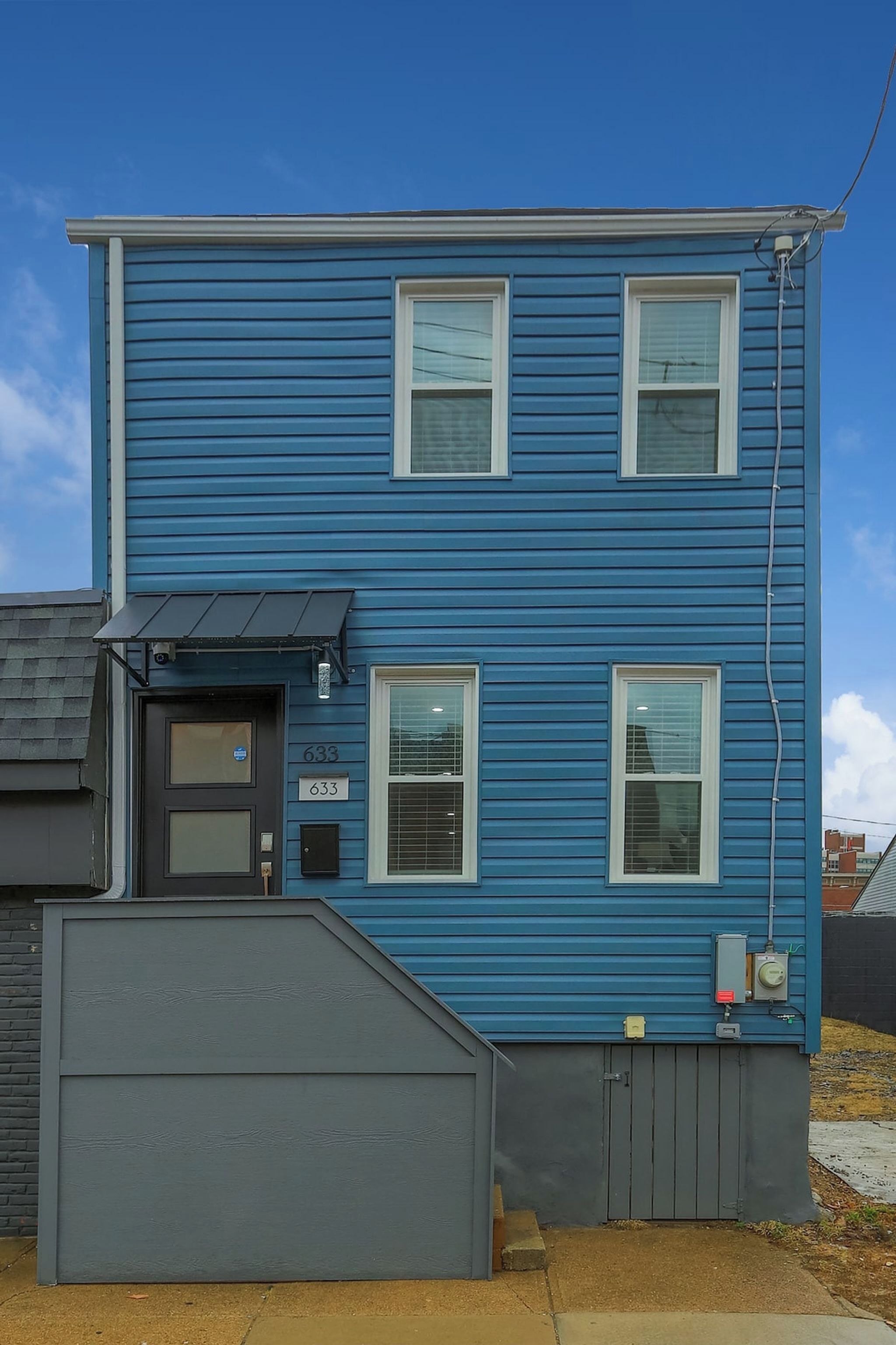 A two-story blue building with a garage, a door with a window, and a small awning.