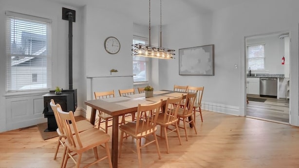 A dining area with a wooden table and chairs, a hanging light fixture, a clock, and a view of the kitchen through an open door. - Modern & Spacious 4BD House in Pittsburgh with Free Street Parking (Pittsburgh)