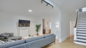 A modern living room with a grey sofa, a dining area, and a staircase. - Modern & Spacious 4BD House in Pittsburgh with Free Street Parking (Pittsburgh)