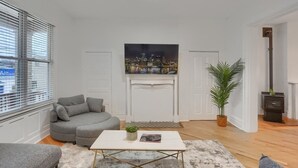A modern living room with a gray sofa, a white fireplace, a cityscape painting, and a potted plant. - Modern & Spacious 4BD House in Pittsburgh with Free Street Parking (Pittsburgh)