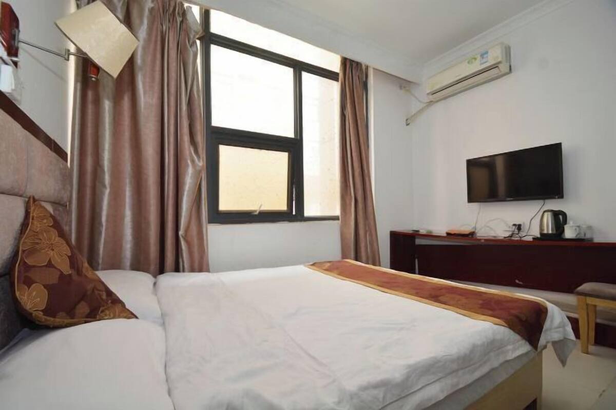 A hotel room with a bed, curtains, a television, and an air conditioning unit.