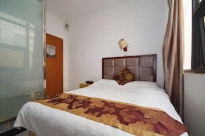 A hotel room with a bed, a nightstand, a lamp, a window with curtains, and a door.