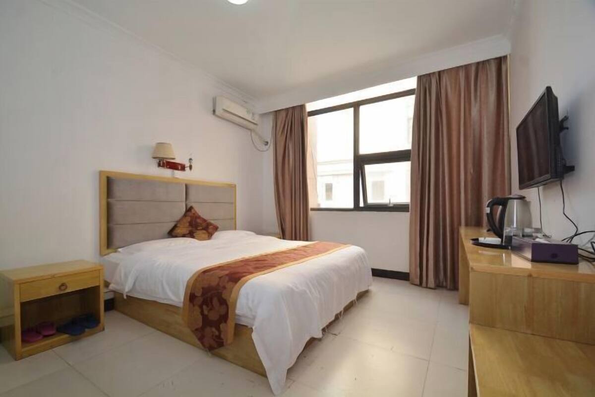 A hotel room with a bed, bedside table, TV, and a window with curtains.