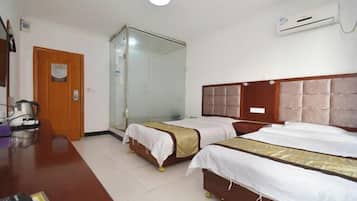 A hotel room with two beds, a wooden desk, a coffee maker, a glass shower enclosure, and an air conditioning unit.