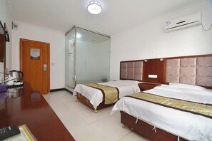 Habitación de hotel con dos camas, un escritorio de madera, cafetera, cabina de ducha de vidrio y aire acondicionado.