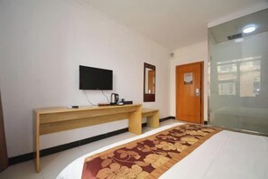 Una habitación de hotel con una cama, un escritorio de madera, un televisor y una puerta.
