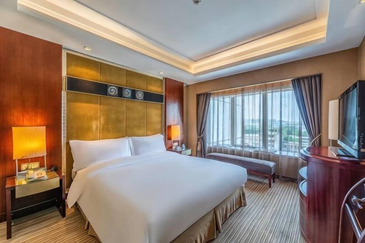Une chambre d’hôtel avec un grand lit, des tables de chevet, une télévision et une fenêtre avec des rideaux.