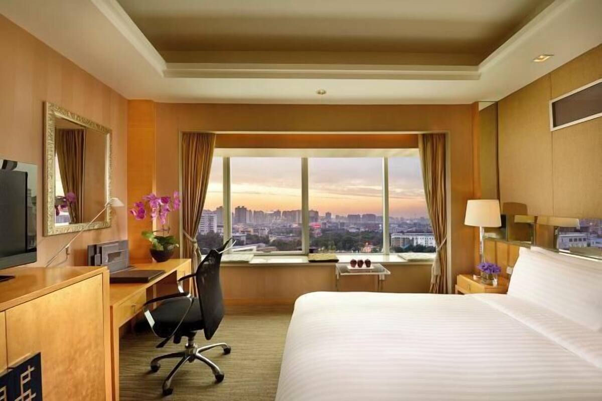 Une chambre d’hôtel avec un lit, un bureau, une chaise, une télévision et une vue sur la ville.