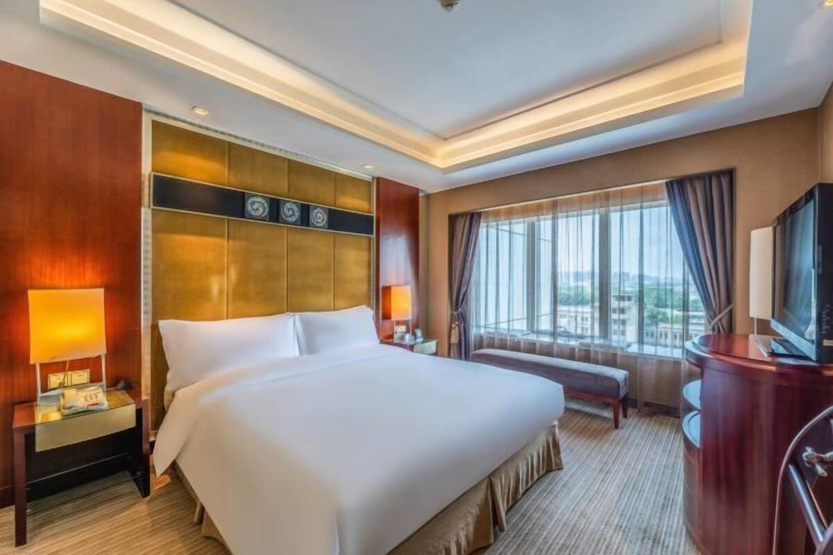 Une chambre d’hôtel avec un grand lit, un bureau, une télévision et une fenêtre avec des rideaux.