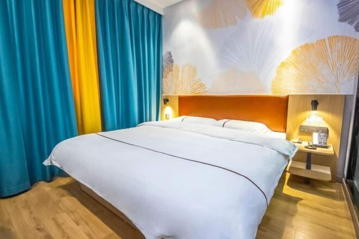 A hotel room with a bed, curtains, a wall with a fan-like pattern, and a bedside table with a lamp.