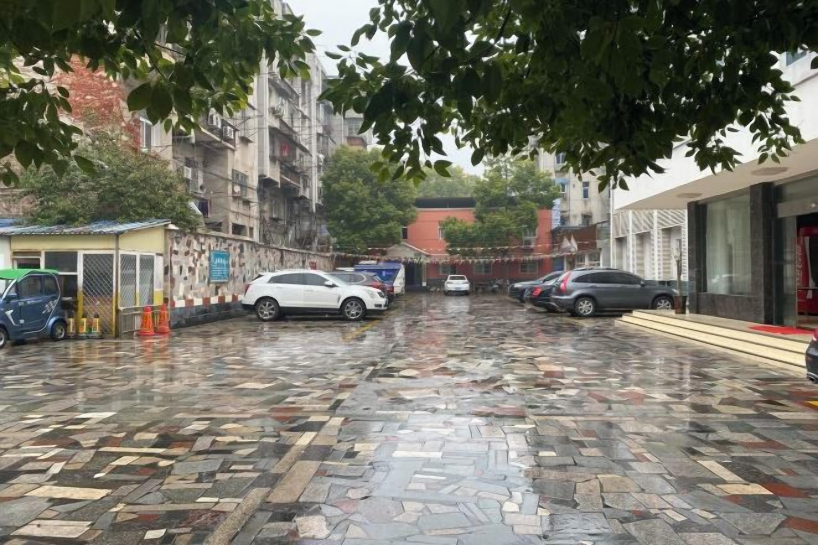 Una àrea de pàrquing amb cotxes, un petit quiosc i edificis al fons.