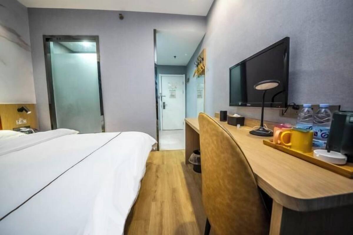 A hotel room with a bed, desk, chair, television, and a door leading to another room.