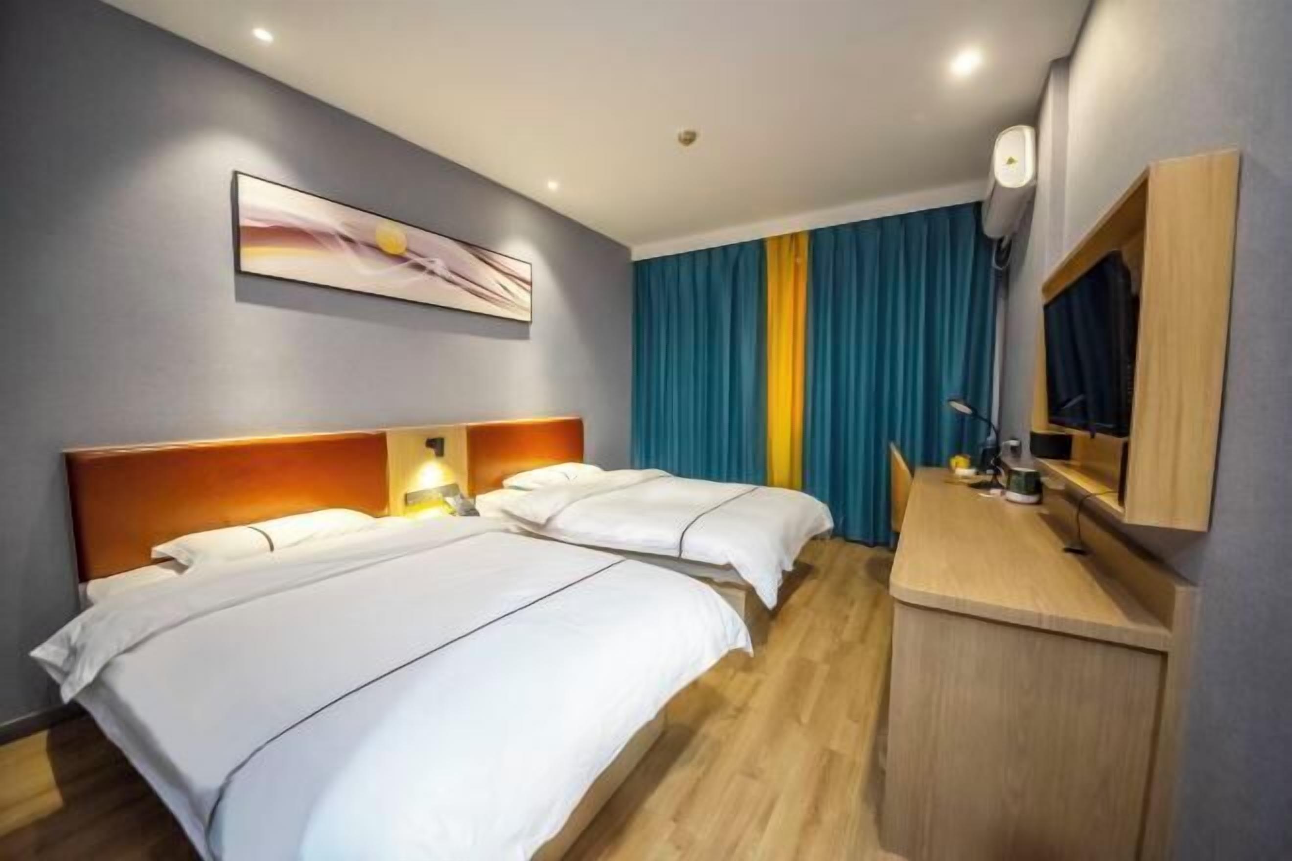 Ein Hotelzimmer mit zwei Betten, einem Holztisch, einem Flachbildfernseher und einem Bild an der Wand.
