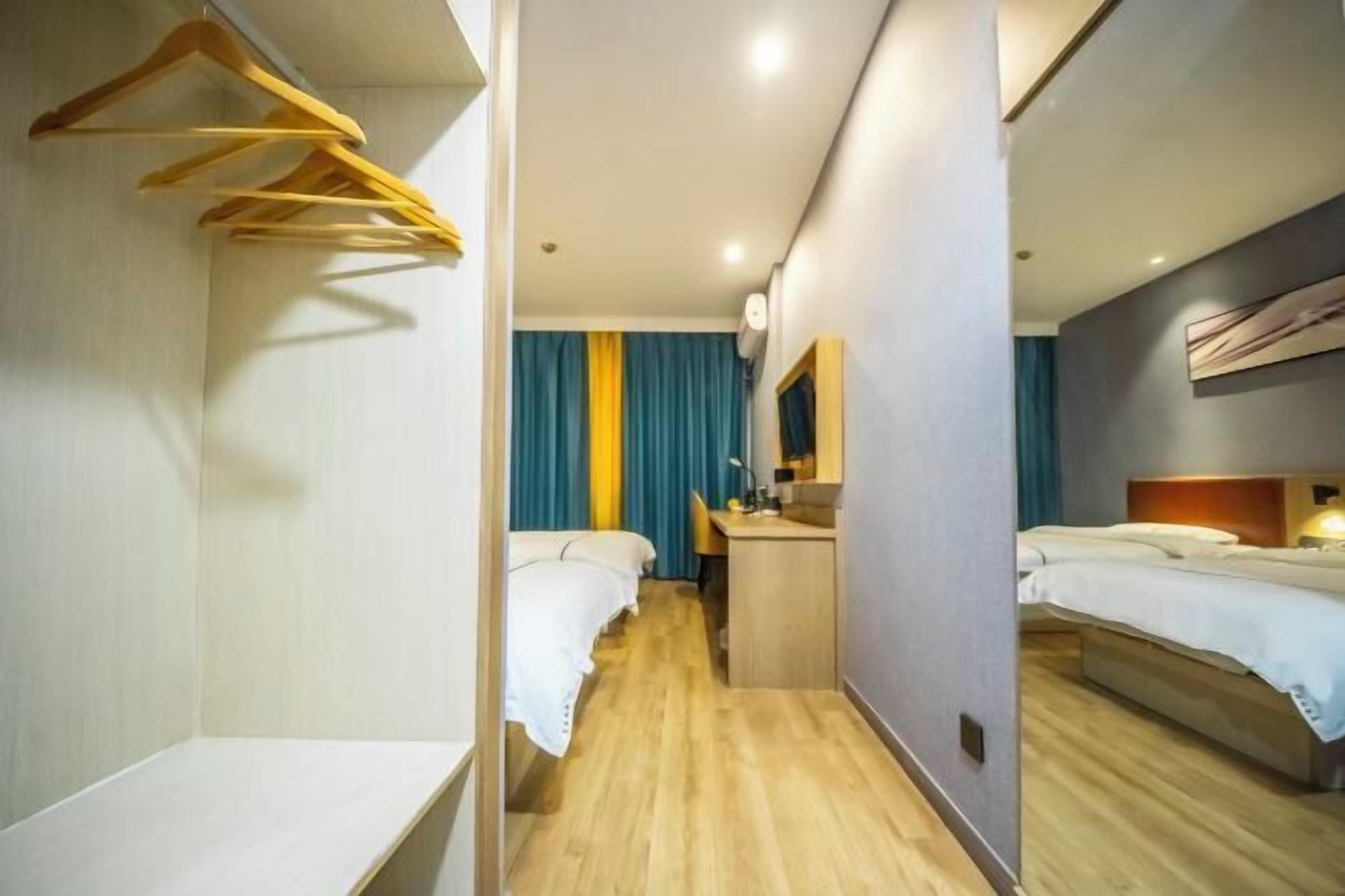 A hotel room with a wooden floor, two beds, a desk, a mirror, and a hanging rack.