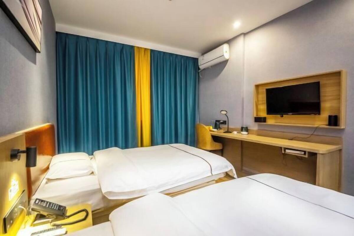 A hotel room with two beds, a desk, a TV, and an air conditioning unit.
