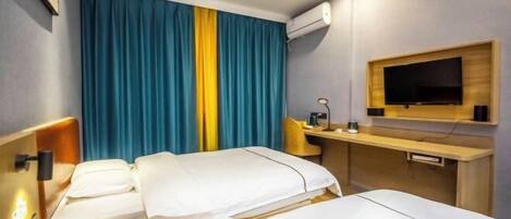 A hotel room with two beds, a desk, a TV, and an air conditioning unit.