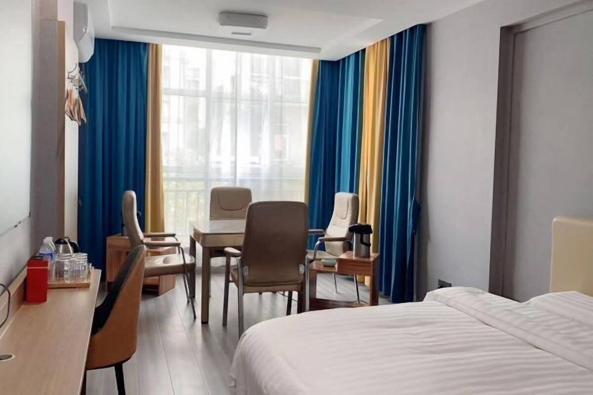 A hotel room with a bed, a desk, a chair, a table, and a window with curtains.