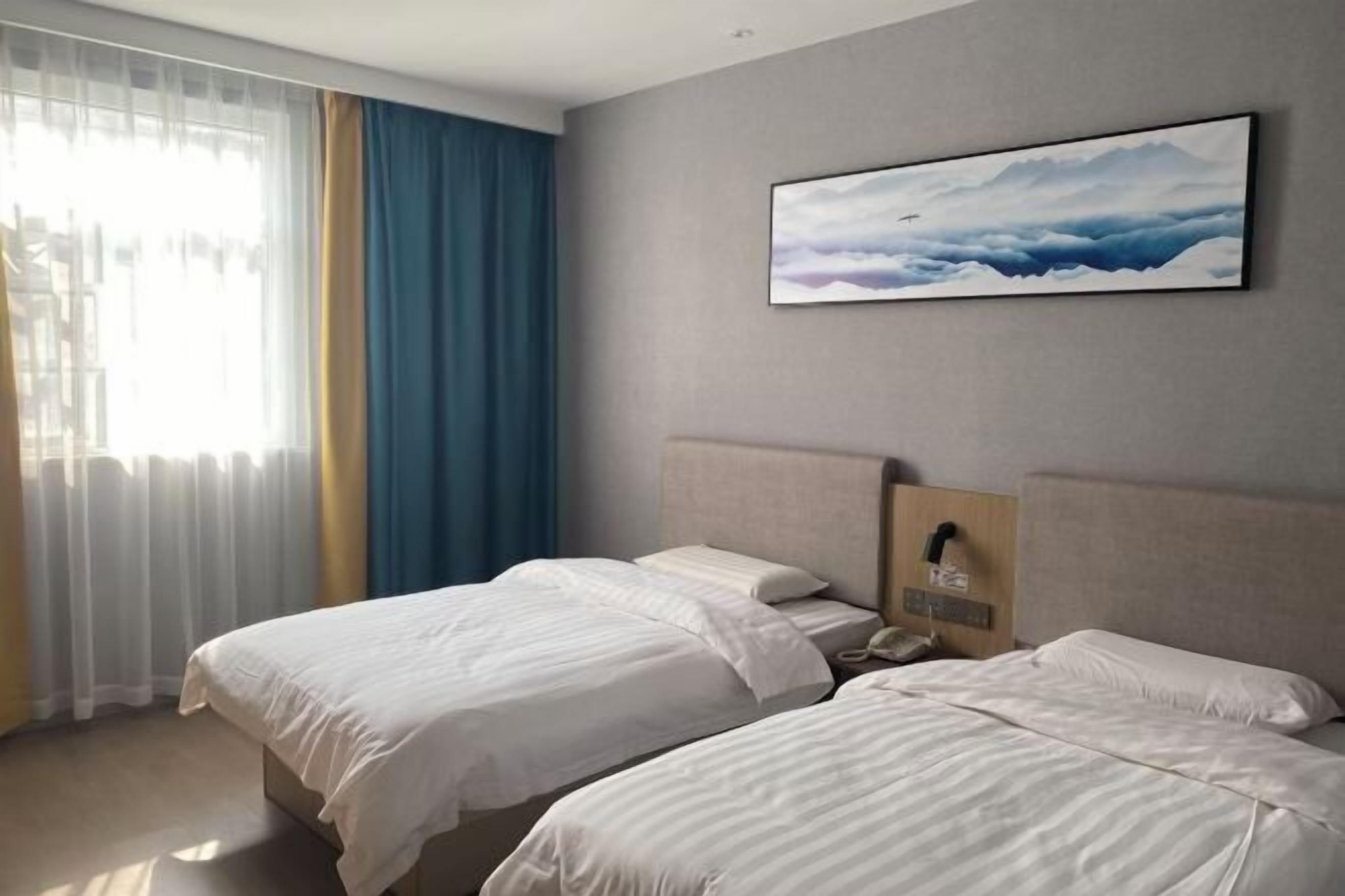 Habitación de hotel con dos camas, un ventanal con cortinas, un cuadro en la pared y un teléfono en la mesita de noche.