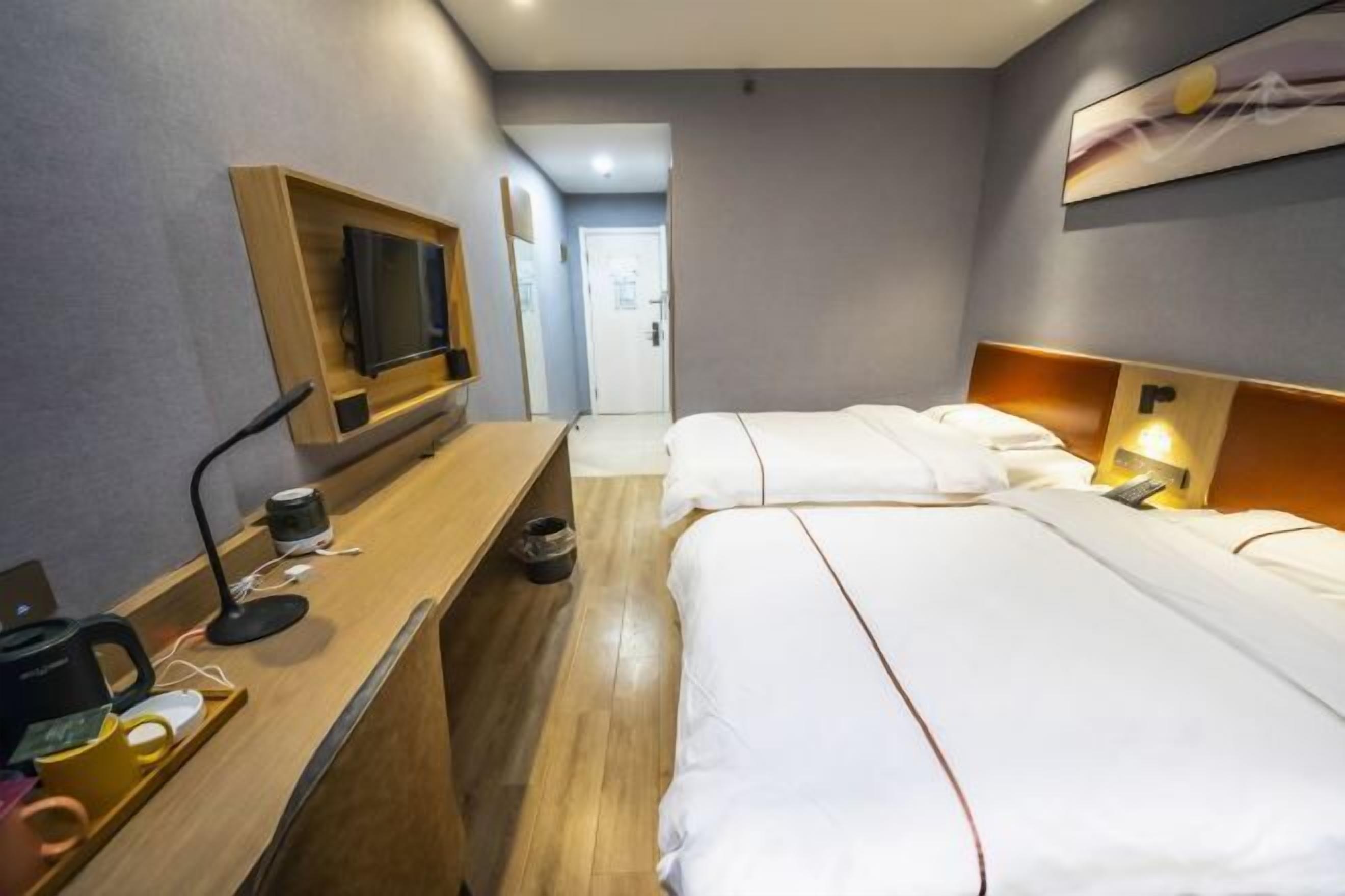 Habitación de hotel con un escritorio de madera, un televisor de pantalla plana, dos camas con ropa blanca y un cuadro en la pared.