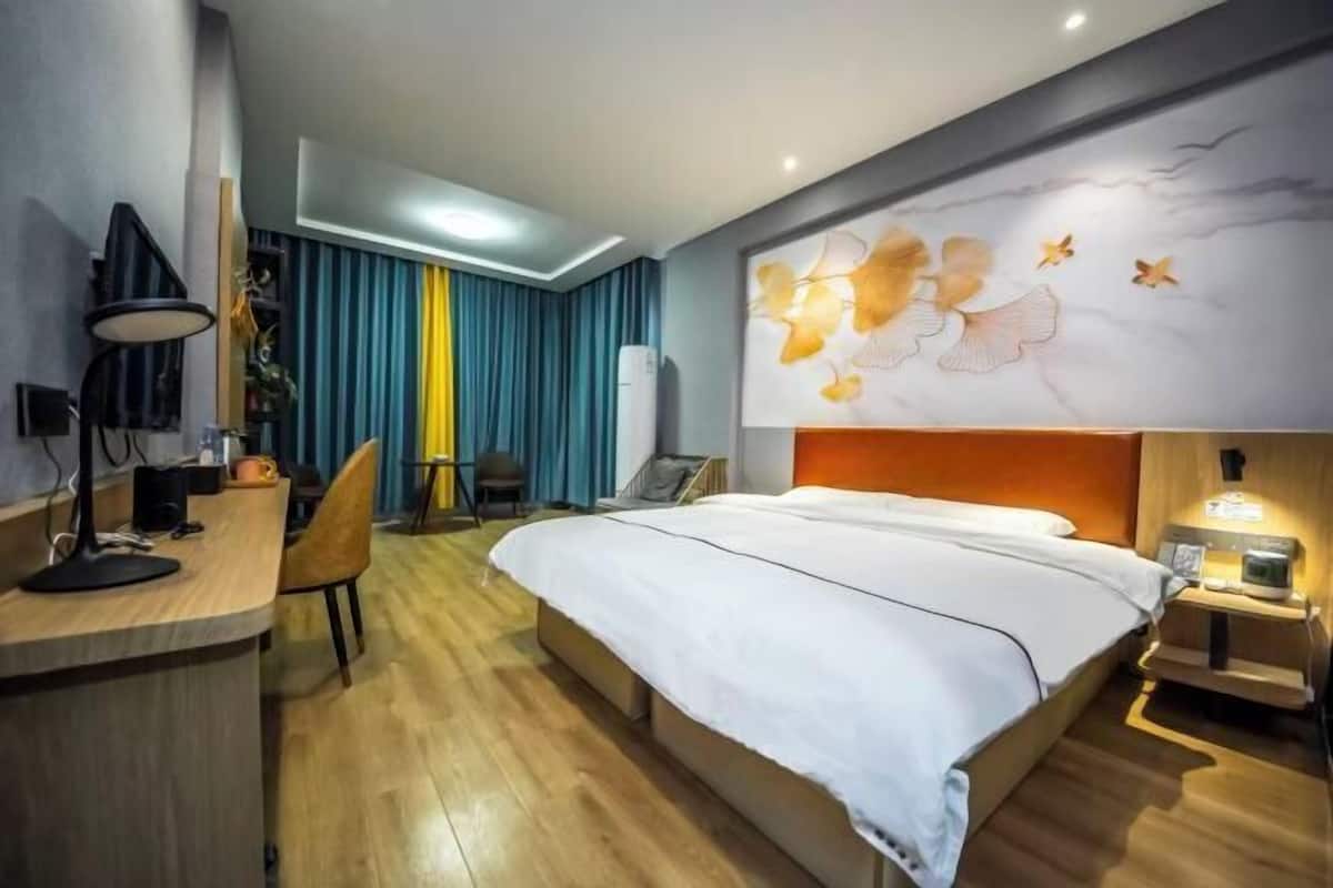 A hotel room with a bed, desk, chair, and a wall with a floral mural.