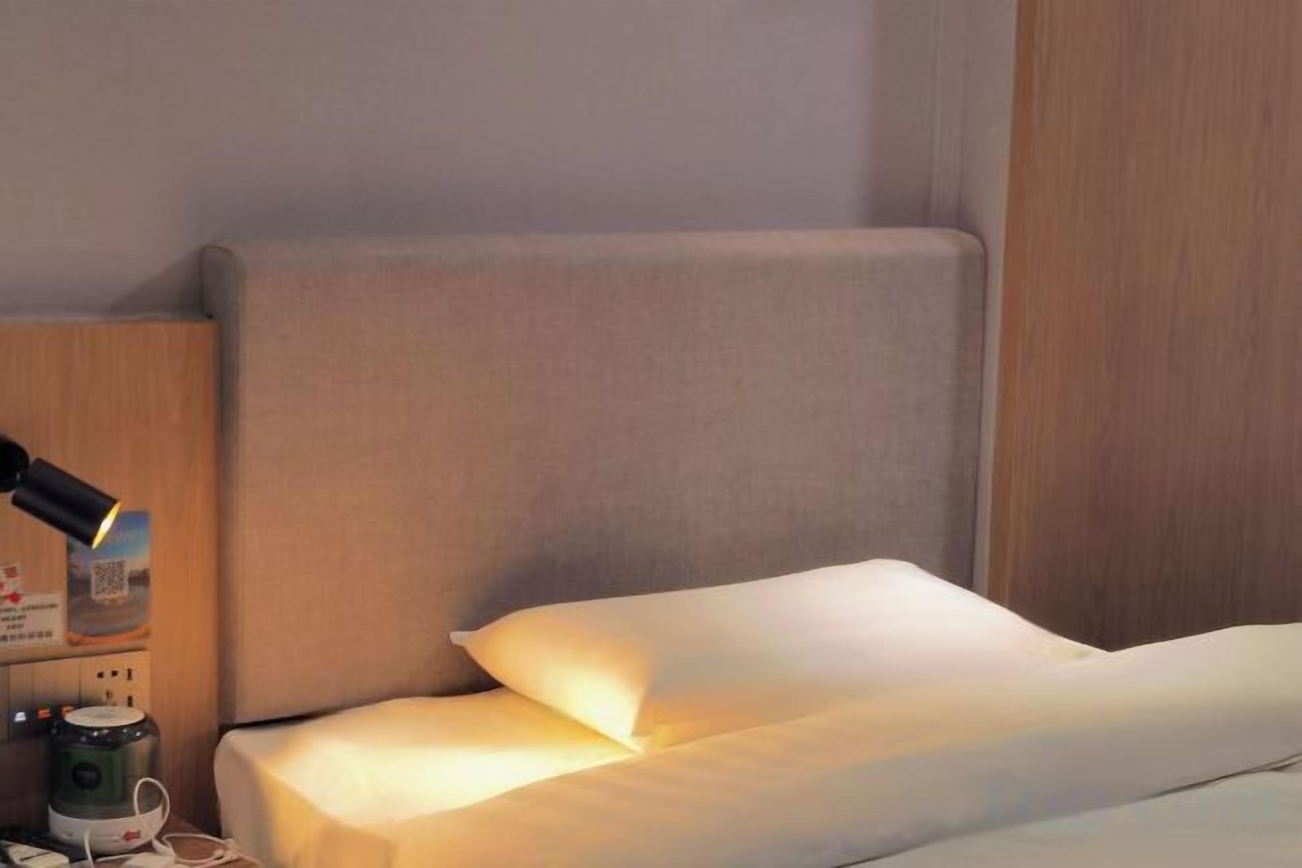 Een bed met hoofdbord, een nachtkastje met een lamp en een koffiezetapparaat.