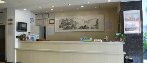 A hotel reception area with a reception desk, framed artwork, and a trash can.