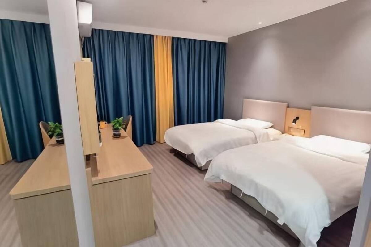 A hotel room with two beds, a desk, and a mirror.