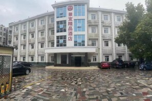 A multi-story hotel with a central entrance, a parking area with several cars, and a tiled ground floor. - Jingyi Boutique Hotel (Anqing Petrochemical No.1 Middle School) (Anqing)