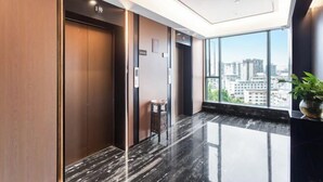 A modern elevator with a wooden finish, a small stool, and a large window offering a city view. - Stone Hotel (Kaili Downtown Wanda Plaza) (Kaili)