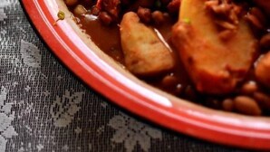 Une vue rapprochée d’un plat composé de pommes de terre, de haricots et de viande, agrémenté d’herbes vertes, et servi dans un bol rouge.