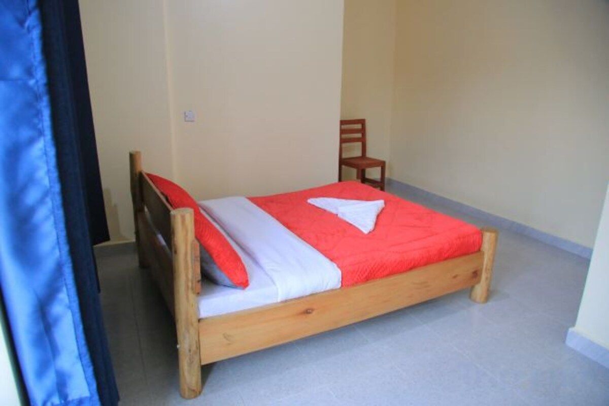 Un lit simple avec une couvre-lit rouge et blanche, une tête de lit en bois et une chaise adossée au mur.