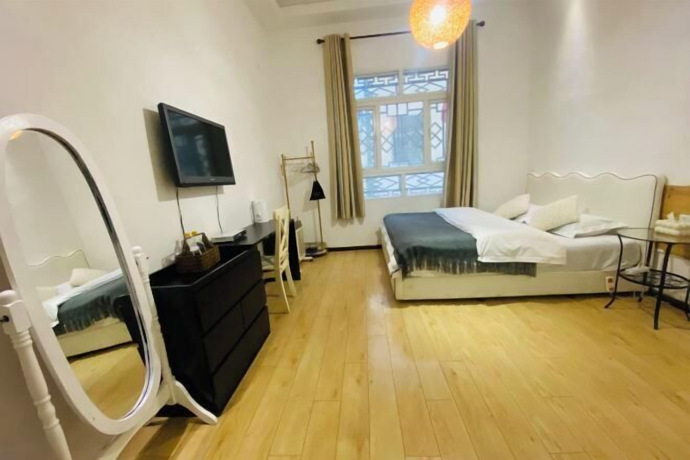 A bedroom with a bed, a television, a mirror, a dresser, and a window with curtains.
