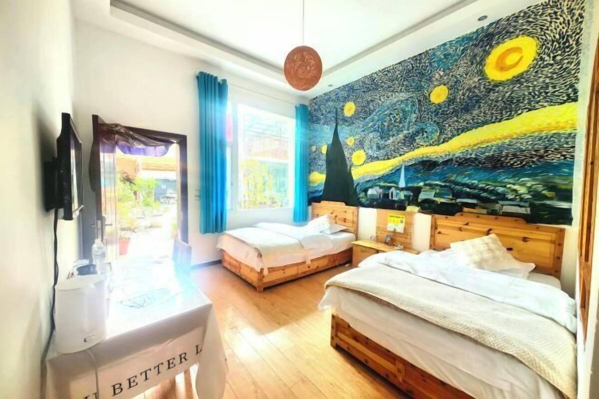 Ein Hotelzimmer mit zwei Betten, einem großen Fenster und einem berühmten Gemälde an der Wand.