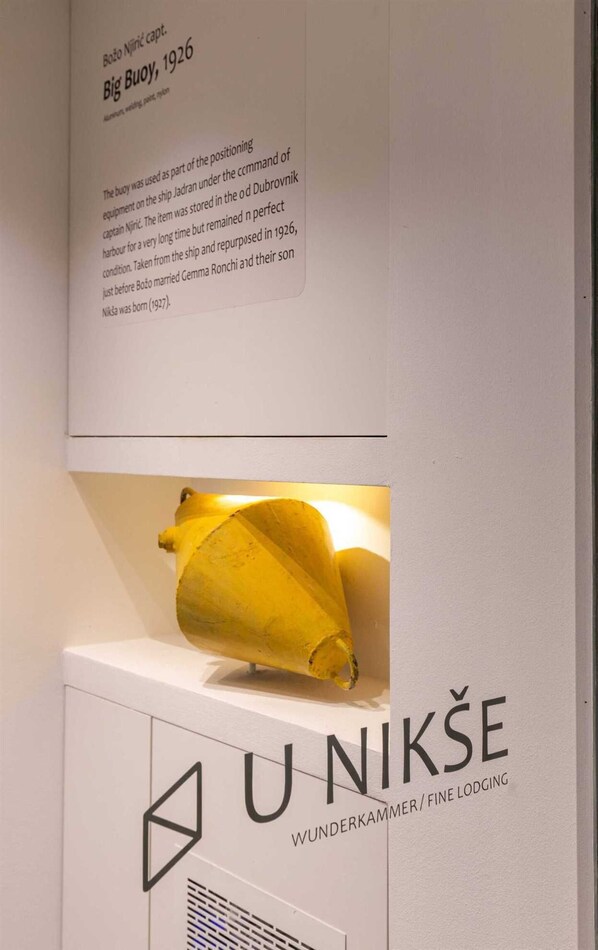 Une exposition d’un objet jaune accompagnée d’un texte relatant son histoire et d’une enseigne indiquant « U NIKSE WUNDERKAMMER/FINE LODGING ».
