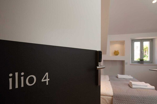 A hotel room with a bed, a window, and a door labeled "ilio 4". - Old Town Apartments U Nikše - Deluxe Studio with City View (Dubrovnik)