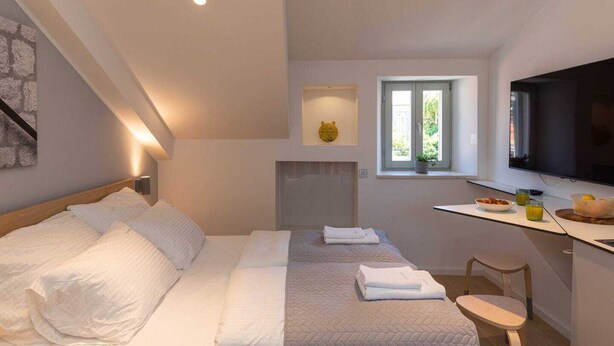 Ein Schlafzimmer mit Bett, Schreibtisch, Flachbildfernseher, Fenster und Kamin.