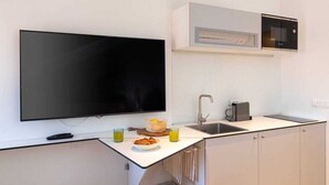 Eine kompakte Küche mit Flachbildfernseher, Mikrowelle, Spüle und einer kleinen Arbeitsfläche mit einer Schüssel voller Speisen und Getränke.