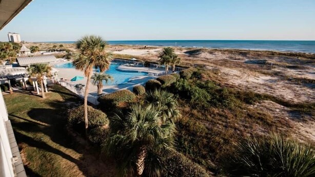 A view of a beach resort with a swimming pool, palm trees, and a clear sky. - Gulf Shores Plantation 3305 (Gulf Shores)