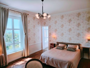 Un dormitorio con cama, mesita de noche, lámpara, ventana con cortinas y candelabro.