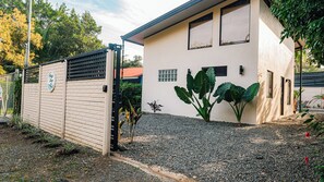 Un edificio con fachada color beige, entrada protegida por una reja y un pequeño jardín con piedras y plantas.