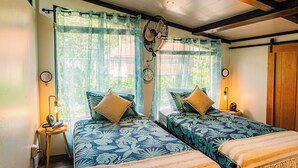 Quarto com duas camas, um ventilador de teto, um relógio e uma mesinha de cabeceira com abajur.