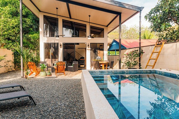 Una casa moderna con piscina, mobiliario de exterior y un porche cubierto.