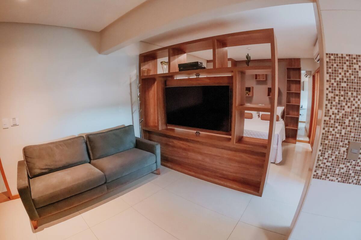 Uma sala de estar com um sofá cinzento, uma unidade de entretenimento de madeira com uma TV de tela plana e piso de azulejos.