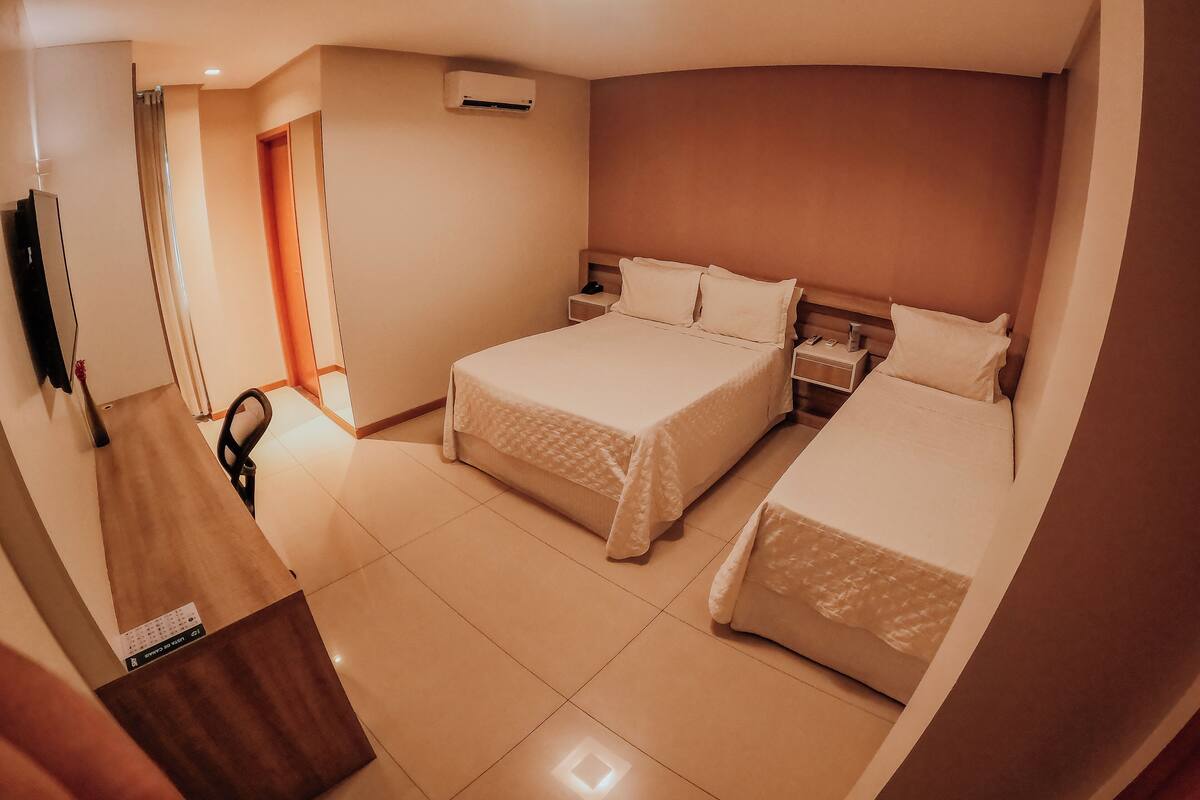 Quarto de hotel com duas camas, uma escrivaninha, uma cadeira, ar condicionado e uma televisão.