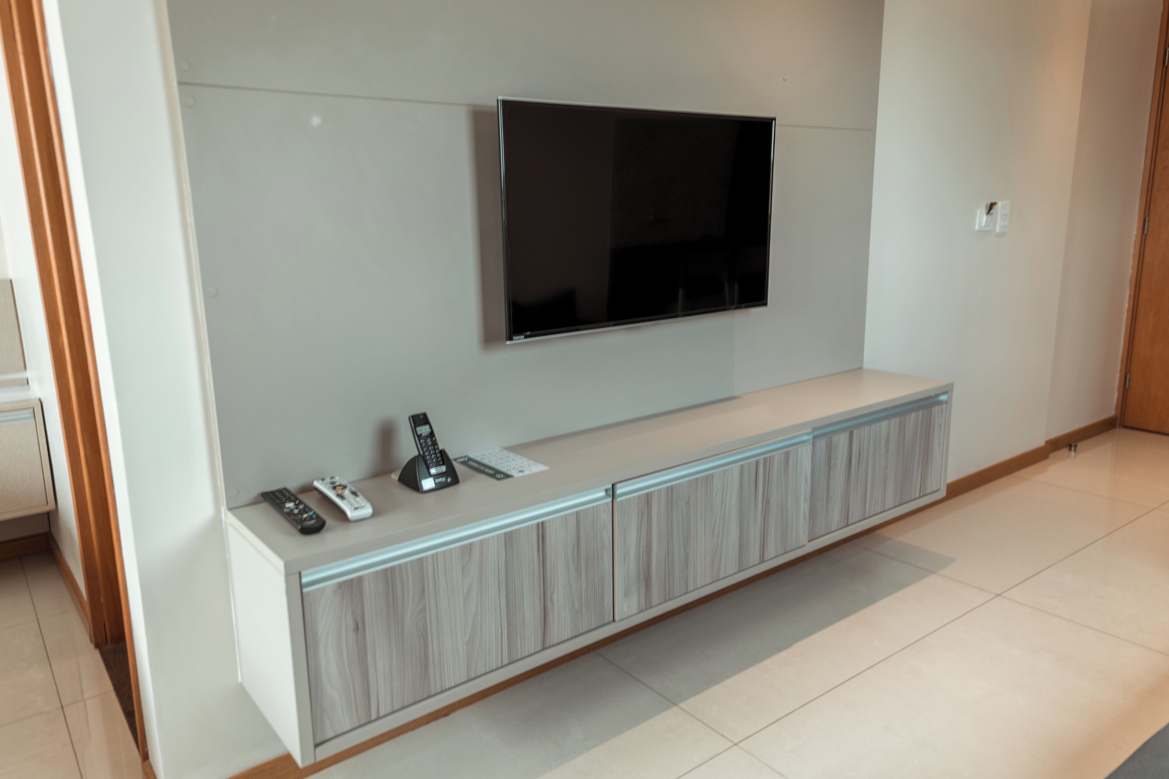 Een moderne woonkamer met een flatscreen televisie aan de muur, een inbouwmeubel met een afstandsbediening, en een telefoon.